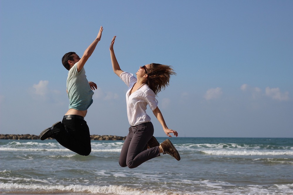 Une femme et un homme sautent en l'air sur la plage et se tapent dans les mains
