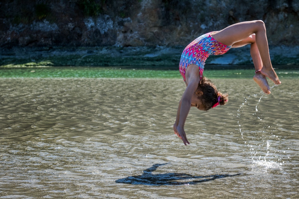 Fillette qui fait de la gymnastique dans l'eau, au bord de la plage