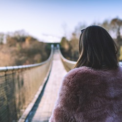 Une jeune femme s'apprête à traverser une vallée sur un pont suspendu